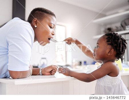 Black child, feeding and mother with spoon in kitchen for food, meal or share together at home. Young African, little girl or kid giving mom a taste of cereal bowl for breakfast, fiber or calcium Black child, feeding and mother with spoon in kitchen for food, meal or share together at home. Young African, little girl or kid giving mom a taste of cereal bowl for breakfast, fiber or calcium 143646772