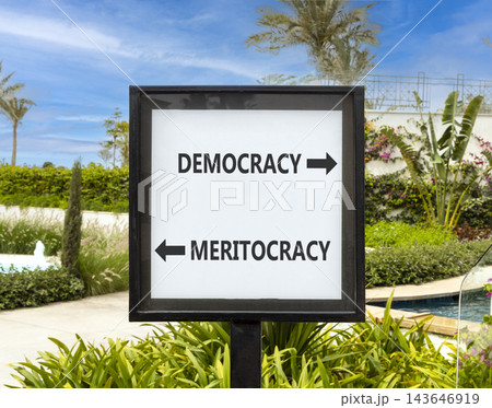 Democracy or meritocracy words symbol. Concept words Democracy Meritocracy on beautiful white road sign. Beautiful palm trees background. Business democracy meritocracy concept. Copy space Democracy or meritocracy words symbol. Concept words Democracy Meritocracy on beautiful white road sign. Beautiful palm trees background. Business democracy meritocracy concept. Copy space 143646919