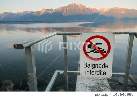 Swimming forbidden sign mounted on railing above serene mountain water Swimming forbidden sign mounted on railing above serene mountain water 143646990