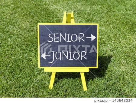 Senior or junior words symbol. Concept words Senior Junior on beautiful yellow blackboard. Beautiful green grass background. Business and senior or junior concept. Copy space. Senior or junior words symbol. Concept words Senior Junior on beautiful yellow blackboard. Beautiful green grass background. Business and senior or junior concept. Copy space. 143648034