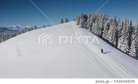 Aerial drone snowboarder climbing a pristine, snow-covered mountain ridge, tranquil forest and breathtaking mountain range, clear blue sky. Bukovel ski resort. Winter nature travel background 143648859