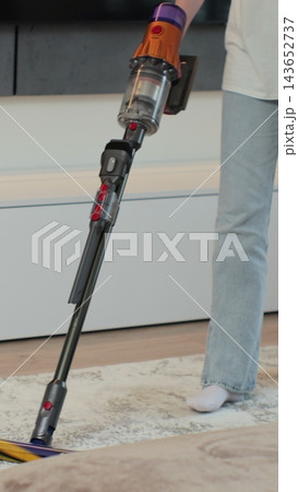 Vertical video. Young woman cleaning carpet with vertical vacuum cleaner in the house. House cleaning concept. Cleaning service. 143652737