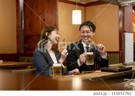 カウンター席で焼き鳥とビールを楽しむ男女 143652762