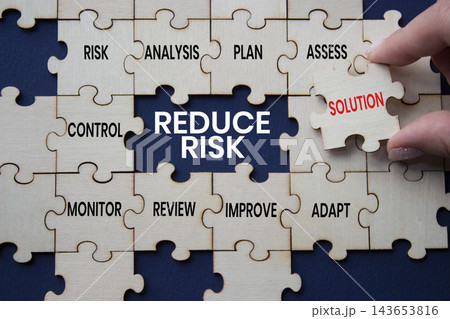 Reduce Risk text on wooden puzzle pieces with solution puzzle piece over deep blue background. Businessman hand. Business risk reduction and strategic planning concept with copy space. Reduce Risk text on wooden puzzle pieces with solution puzzle piece over deep blue background. Businessman hand. Business risk reduction and strategic planning concept with copy space. 143653816