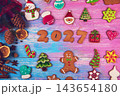 Christmas gingerbread cookies and holiday decorations forming year 2027 on colorful blue and pink wooden background 143654180