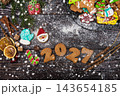 Festive gingerbread cookies for Christmas and New Year 2027 with spices and decorations on a dark wooden table 143654185