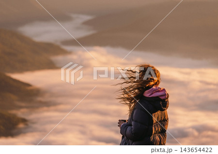 Woman watching sunrise above mountain valley Woman watching sunrise above mountain valley 143654422