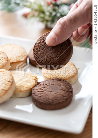 Hand picking up chocolate shortbread cookie from plate with assorted cookies 143654519
