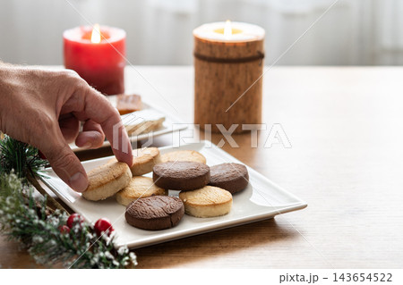 Hand picking up chocolate shortbread cookie from plate with assorted cookies Hand picking up chocolate shortbread cookie from plate with assorted cookies 143654522