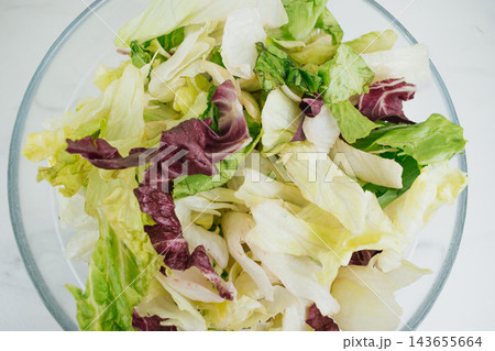 Top down view of fresh mixed lettuce leaves and purple radicchio salad in transparent glass bowl on white table background for healthy diet stock photo Top down view of fresh mixed lettuce leaves and purple radicchio salad in transparent glass bowl on white table background for healthy diet stock photo 143655664