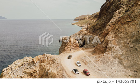 Aerial view of cars driving slowly along dusty dirt road on steep rocky coast heading toward Balos beach on Gramvousa peninsula Crete Greece Aerial view of cars driving slowly along dusty dirt road on steep rocky coast heading toward Balos beach on Gramvousa peninsula Crete Greece 143655701
