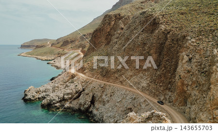 Drone view of narrow unpaved dirt road carved into steep rocky cliff along sea coast on route to Balos lagoon in Gramvousa Crete Greece Drone view of narrow unpaved dirt road carved into steep rocky cliff along sea coast on route to Balos lagoon in Gramvousa Crete Greece 143655703