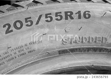 Close-Up of 205-55 R16 Studded Winter Tire Sidewall Showing Tire Size Markings and Metal Studs 143656793