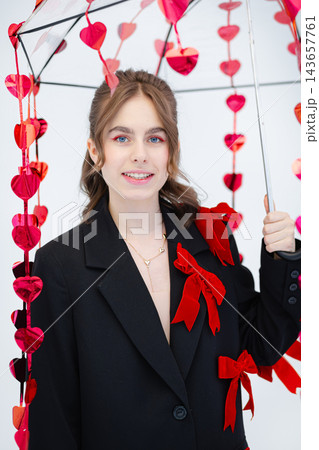 Young woman holding umbrella decorated with red heart garlands wearing black blazer with red bows and heart necklace Young woman holding umbrella decorated with red heart garlands wearing black blazer with red bows and heart necklace 143657761