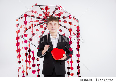 Boy dressed formally holds heart-shaped box and transparent umbrella  143657762