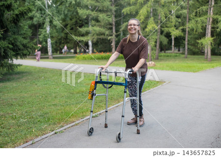 A young woman with cerebral palsy walks in a park with a walker. A young woman with cerebral palsy walks in a park with a walker. 143657825