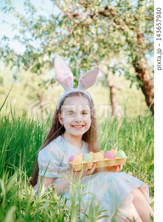 Happy girl wearing bunny ears sits smiling holding colorful Easter Happy girl wearing bunny ears sits smiling holding colorful Easter 143657980