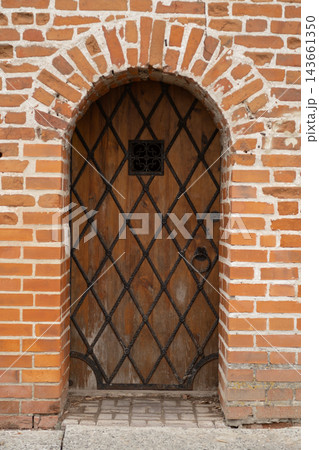 Rustic wooden door features a diamond pattern and wrought iron accents, framed by a brick wall, highlighting traditional architectural details 143661350
