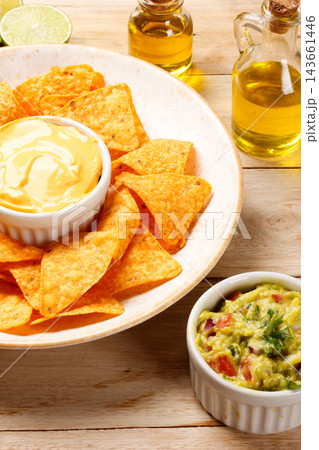 Crispy tortilla nachos on a rustic plate with creamy cheddar cheese sauce and guacamole, on a wooden table. Crispy tortilla nachos on a rustic plate with creamy cheddar cheese sauce and guacamole, on a wooden table. 143661446
