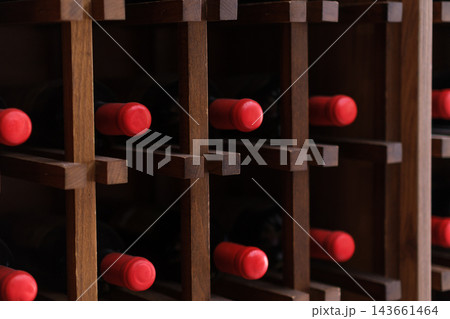 Dark wooden rack displays multiple red bottle necks extending through square compartments, creating a repeated geometric storage pattern 143661464