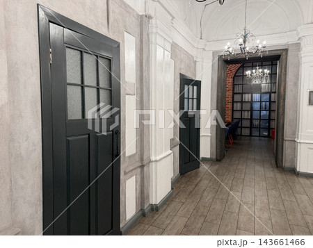Interior hallway features gray walls and wooden flooring, with black doors on either side leading to rooms and elegant chandeliers above 143661466