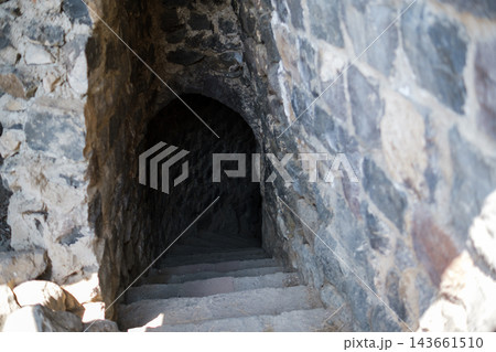 Stone steps descend into a dimly lit passageway inside Bjni Fortress, surrounded by rough stone walls and historical architectural features Stone steps descend into a dimly lit passageway inside Bjni Fortress, surrounded by rough stone walls and historical architectural features 143661510
