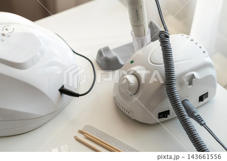 Professional manicure tools displayed on a white table, featuring a UV lamp, electric nail drill, nail files, and wooden sticks for nail care 143661556