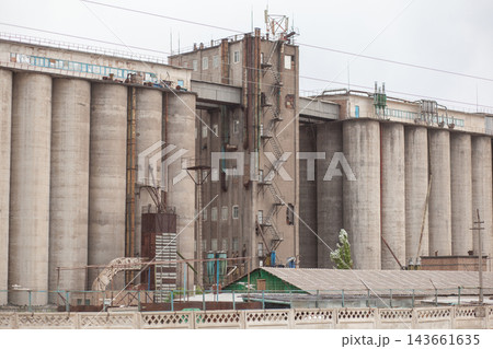 Industrial grain storage facility featuring tall concrete silos and a metal staircase, with a green structure visible in the foreground Industrial grain storage facility featuring tall concrete silos and a metal staircase, with a green structure visible in the foreground 143661635