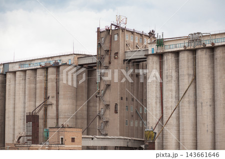 Industrial grain storage facility features large silos and exterior staircases, set against a cloudy sky in an urban landscape Industrial grain storage facility features large silos and exterior staircases, set against a cloudy sky in an urban landscape 143661646