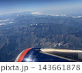 Rugged mountain ranges with scattered snow fill the landscape beyond a passenger aircraft wing, viewed from high altitude through clear blue air 143661878