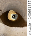 Round earthen shaft descends into darkness around a smaller central opening, revealing rough soil walls and a sunlit sandy surface 143661887