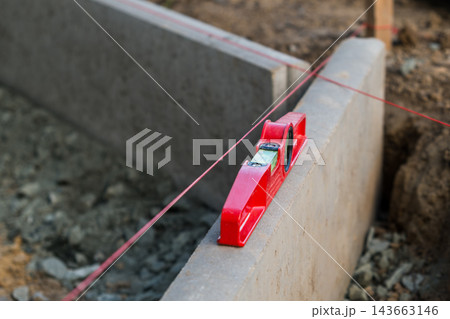 In a construction environment, a leveling tool rests on a concrete block aligned with a string line. In a construction environment, a leveling tool rests on a concrete block aligned with a string line. 143663146