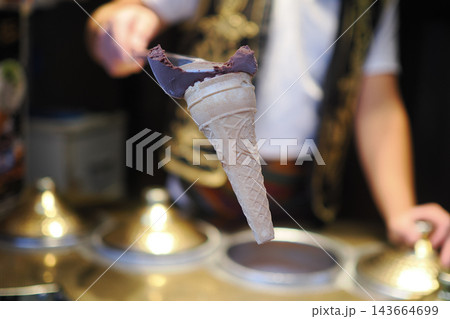 Scooping ice cream cone at a food stand in a lively market scene Scooping ice cream cone at a food stand in a lively market scene 143664699