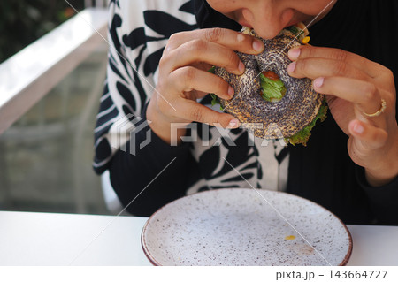 A woman is eating a sandwich made with a black bun at a cafe 143664727