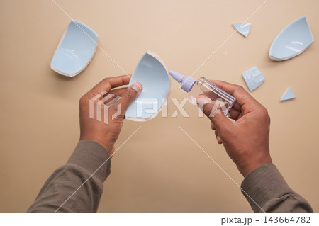 Hands repairing broken ceramic bowl with glue on beige surface Hands repairing broken ceramic bowl with glue on beige surface 143664782