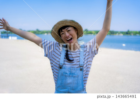 Woman celebrating summer vacation at beach with arms raised 143665491