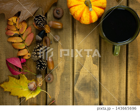 Autumn Coffee Corner with Dark Mug, Orange Pumpkin, Pinecones and Colorful Leaves on Wooden Table, October Copy Space Background 143665696