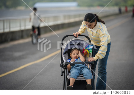 mother adjusting stroller shade for sleepy or headache little daughter outdoors on road mother adjusting stroller shade for sleepy or headache little daughter outdoors on road 143665813