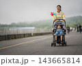 mother walking with child girl sleeping in stroller along the road 143665814