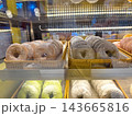 A variety of colorful donuts dusted with powdered sugar are neatly arranged in rows within woven baskets inside a glass bakery display case at a cafe or pastry shop. 143665816
