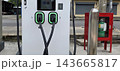Modern electric vehicle charging station on an urban sidewalk with two cables docked. Glowing green lights indicate readiness for sustainable transit power. 143665817