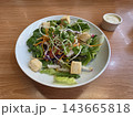 A fresh garden salad with mixed greens, croutons, and sunflower sprouts in a white bowl, served with creamy dressing on a wooden table. 143665818