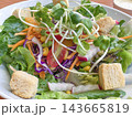 Fresh garden salad served in a white bowl features mixed greens topped with sunflower sprouts, croutons, shredded carrots, red cabbage, and cherry tomatoes for a healthy vegetarian meal. 143665819