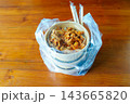 A Korean takeaway food order of spicy meat and rice in paper bowls, packed in a clear plastic bag with chopsticks on a wooden table. Represents food delivery or a convenient office lunch. 143665820