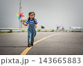 happy preschool child girl walking on road while holding a colorful wind turbine 143665883