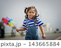 happy preschool child girl walking on road while holding a colorful wind turbine 143665884