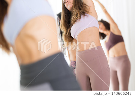 Group of young sporty attractive women in yoga studio, practicing yoga lesson with instructor, standing, stretching and relaxing after workout . Healthy active lifestyle, working out indoors in gym. 143666245
