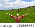 Relaxed fashionable caucasian woman wearing red asian style kimono, arms rised to sky, enjoying pure nature at beautiful green rice fields on Bali island. 143666268