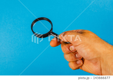 Hand holding a magnifying glass against a blue background Hand holding a magnifying glass against a blue background 143666877