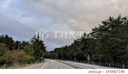 森林に囲まれた緩やかなカーブが続く道路と曇り空 143667190